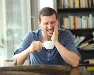 Mann hält sich nach dem Trinken von Kaffee eine Hand an die Wange und verzieht schmerzhaft das Gesicht